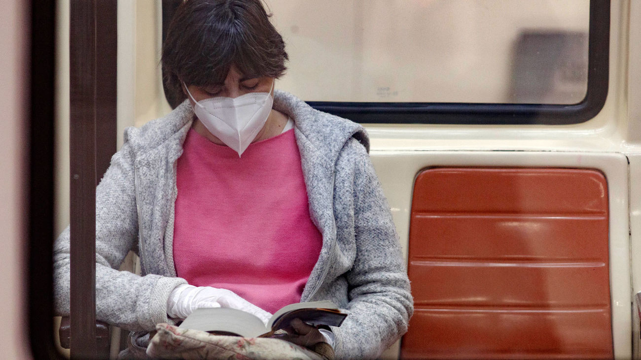 Una pasajera con mascarilla y guantes lee en un vagón del Metro de Madrid