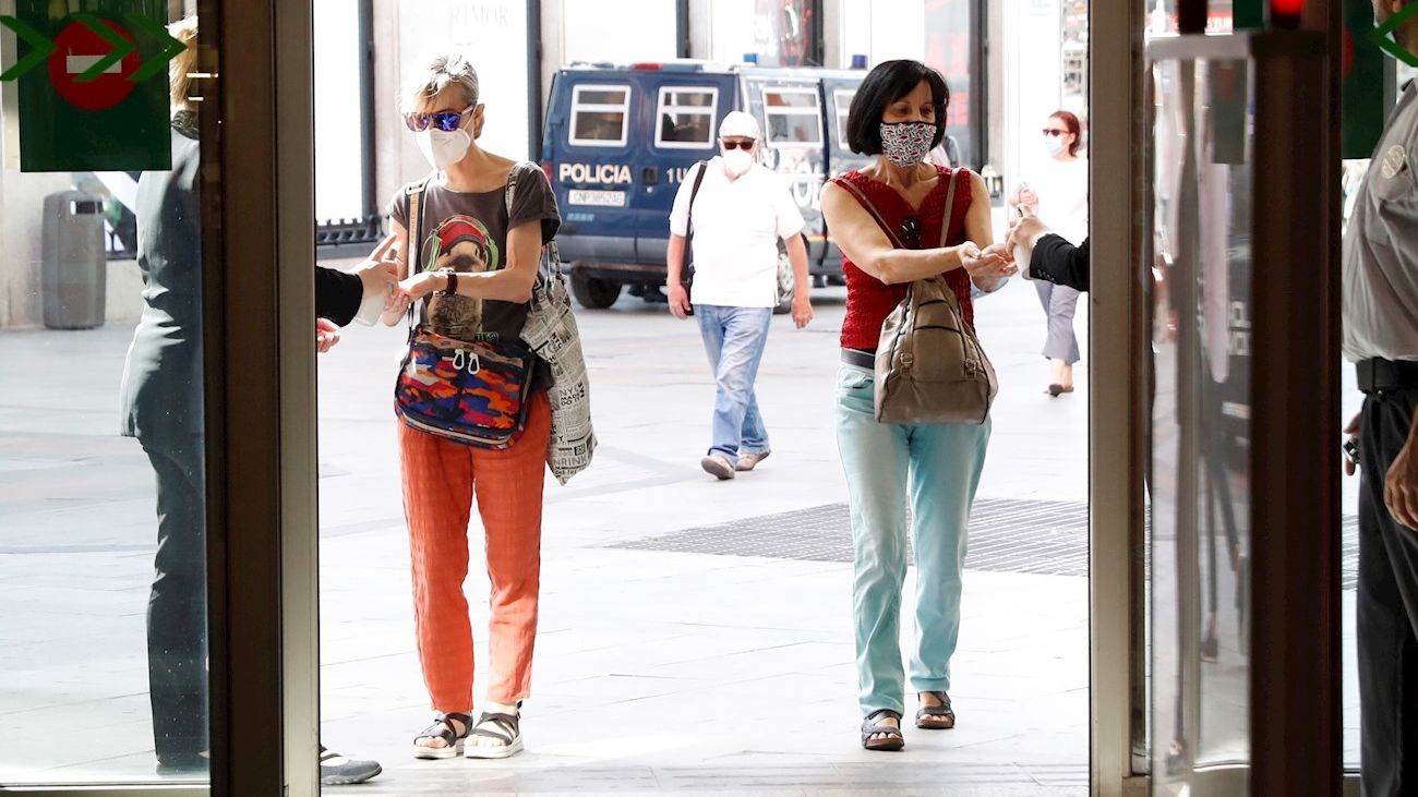 Dos mujeres se aplican desinfectante en las manos antes de entrar a un centro comercial
