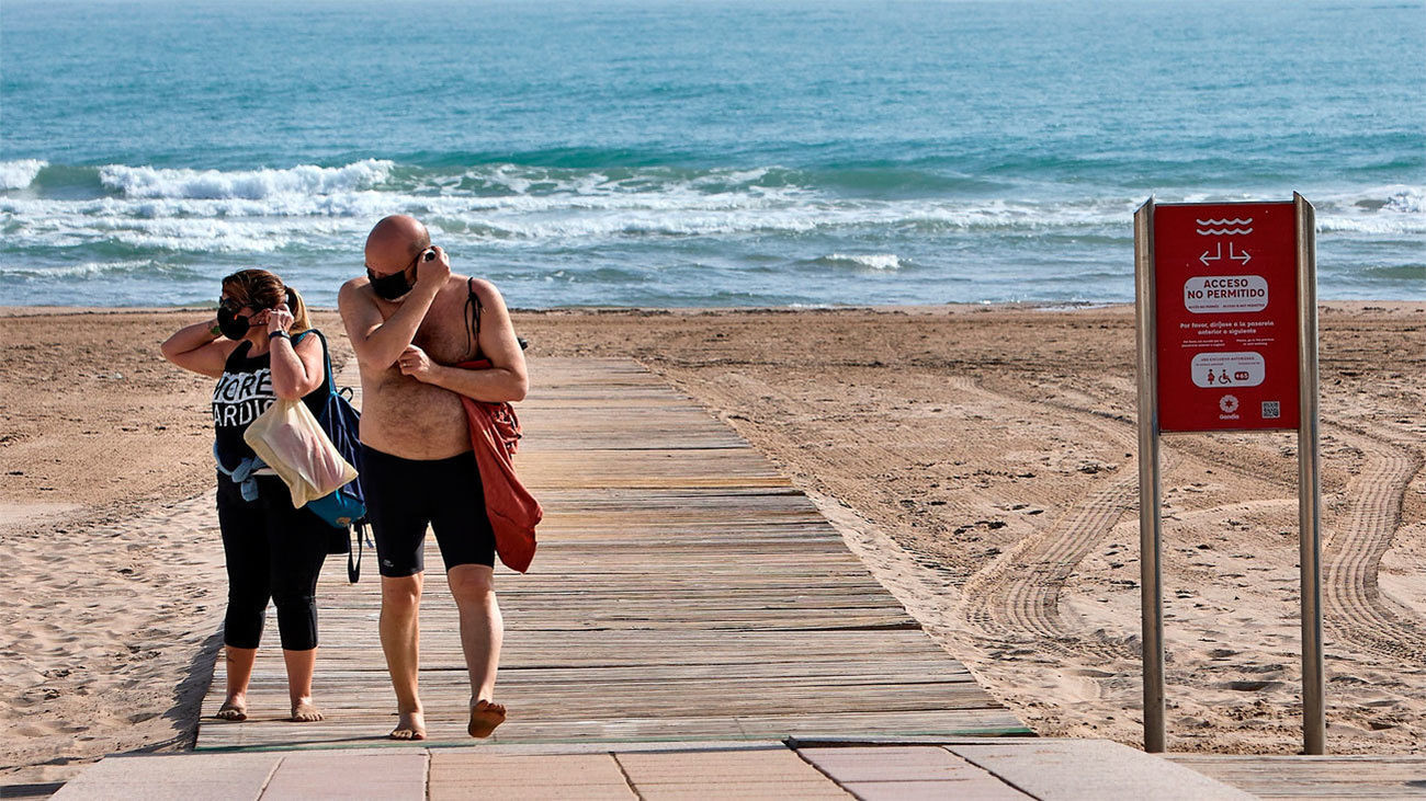Dos personas se colocan las mascarillas mientras caminan por la plataforma de una playa