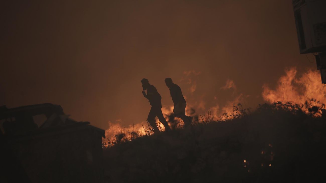 Dos personas caminan cerca de las llamas en uno de los incendios de Grecia
