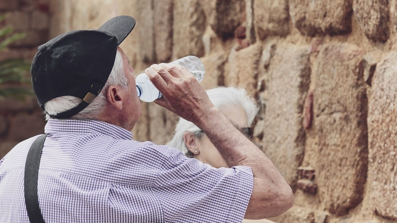 Un hombre mayor bebe agua de una botella en un día de intenso calor