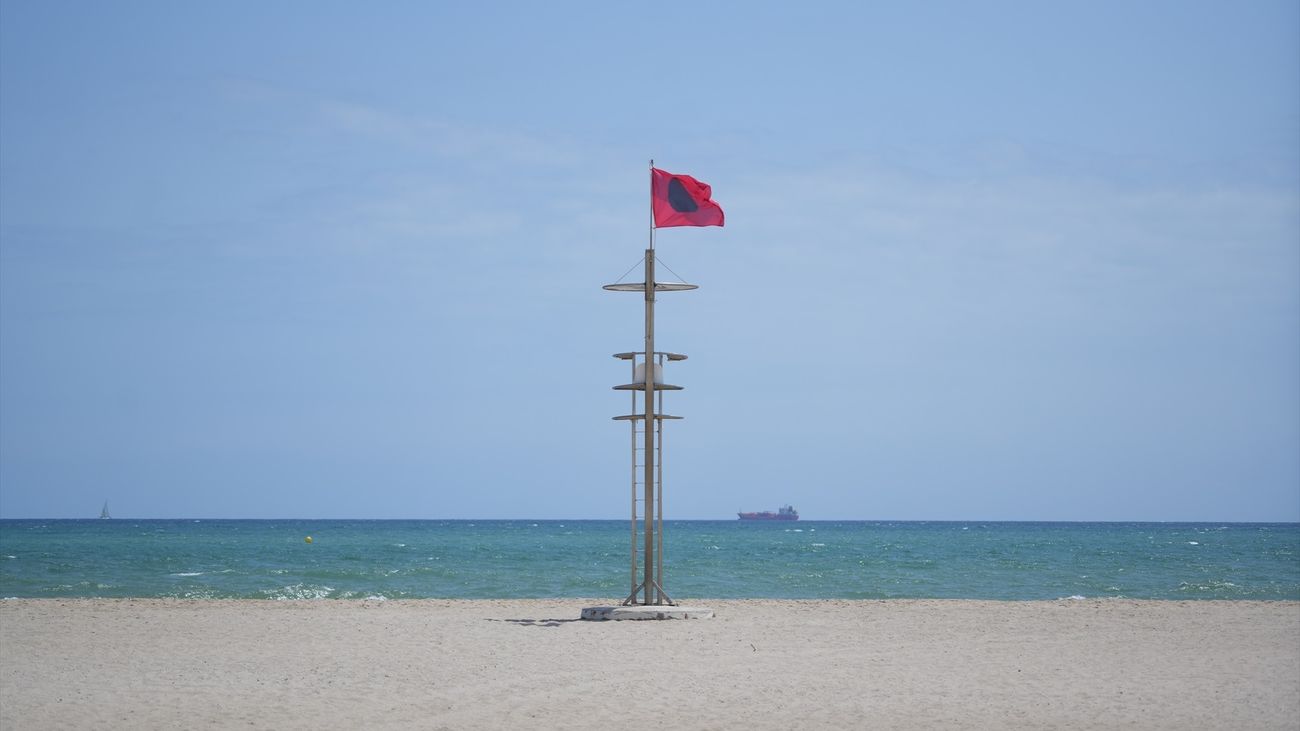 Bandera roja durante las labores de limpieza en la playa del Saler por un vertido