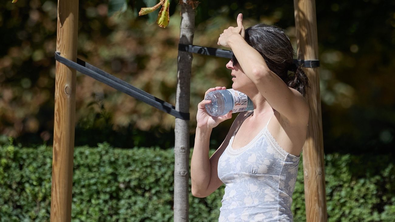 Una mujer se refresca con una botella de agua en el parque de El Retiro