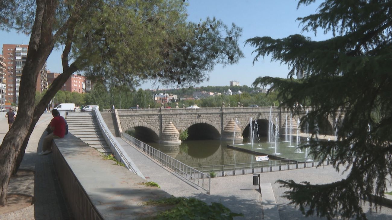 Dos personas se protegen del calor bajo la sombra de un árbol en el entorno de Madrid Río