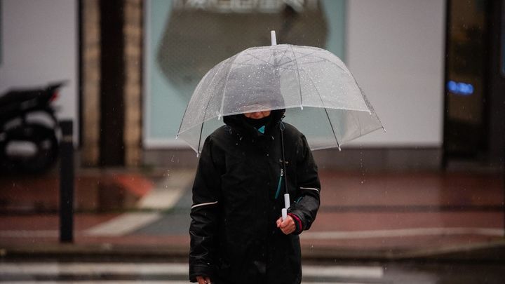 Una persona se protege de la lluvia con paragua, en Madrid