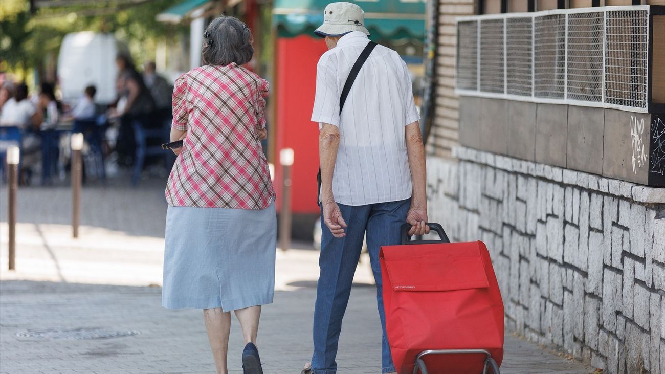 Una pareja mayor camina con un carro de la compra