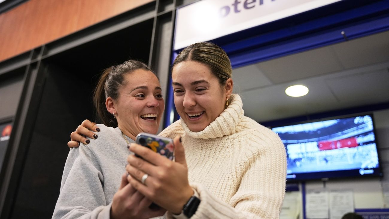 Dos personas sonríen ante un móvil delante de una administración de lotería