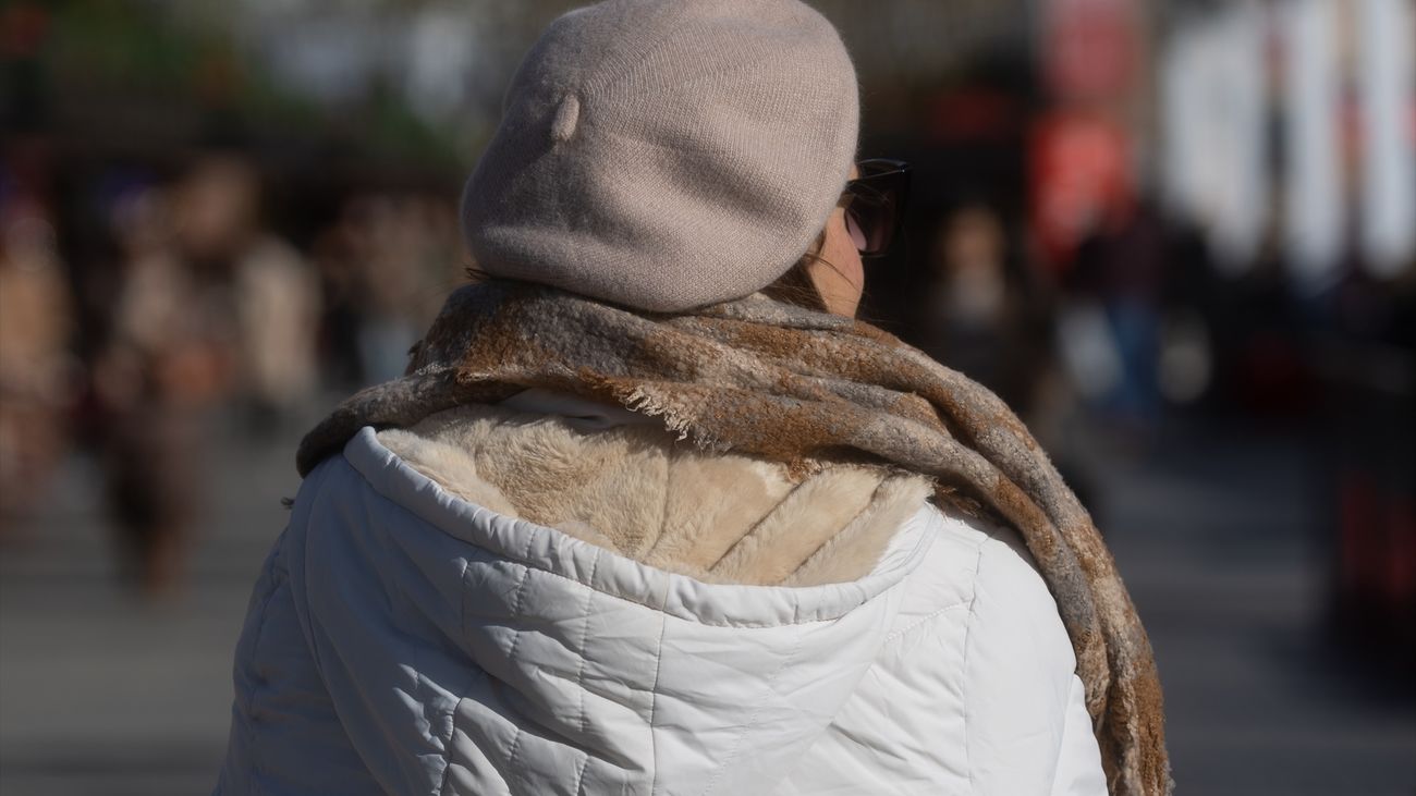 Una mujer abrigada con bufanda y gorro pasea por Madrid